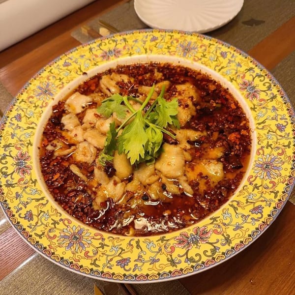 Spicy Chinese fish dish with red chili oil and cilantro in a decorative yellow bowl.