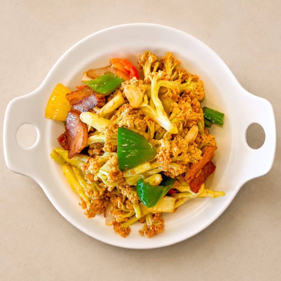 Stir-fried cauliflower with bacon, green and yellow bell peppers, and garlic in a white dish.