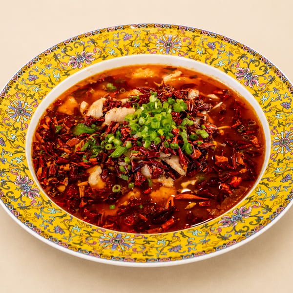 Spicy fish stew with red chili peppers and green onions in a decorative yellow bowl.