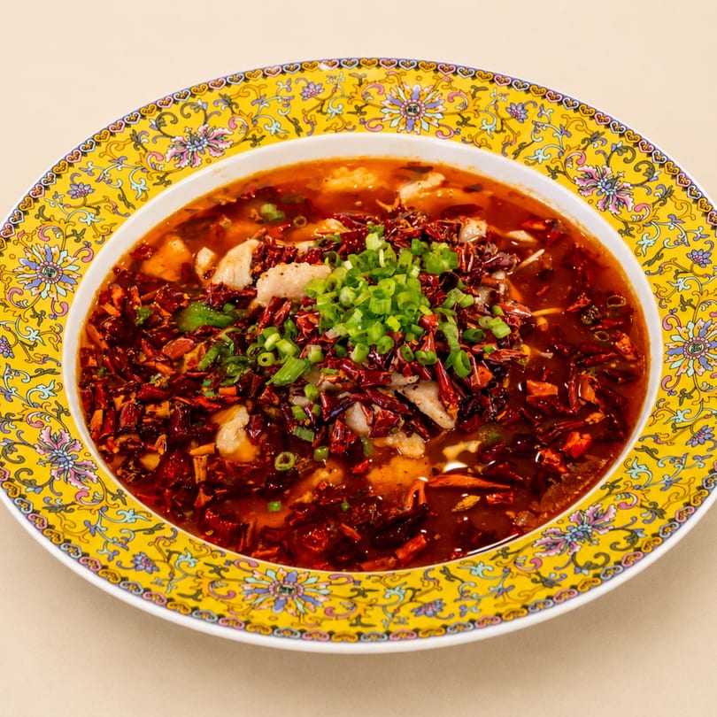 Spicy fish stew with red chili peppers and green onions in a decorative yellow bowl.